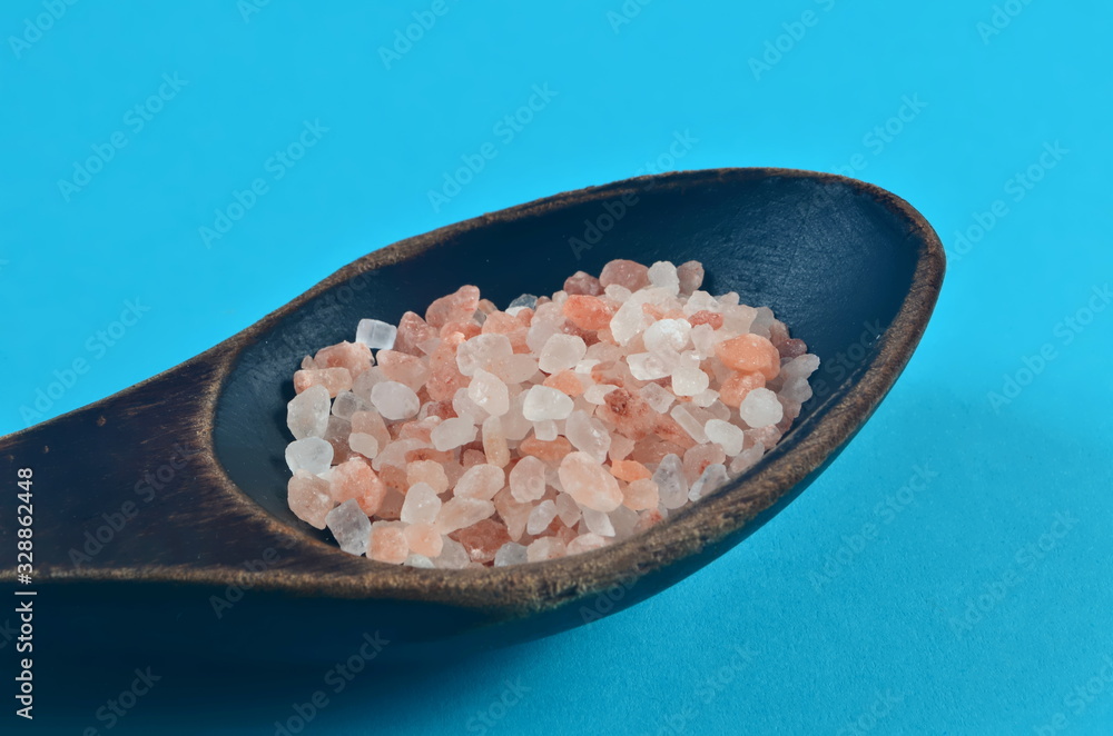 Himalayan pink salt in dark wooden spoon on blue background Himalayan pink salt in dark wooden spoon on blue background