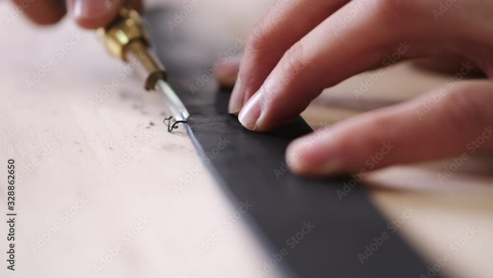 A leather craftsman is cutting the edges of a belt. The master is using