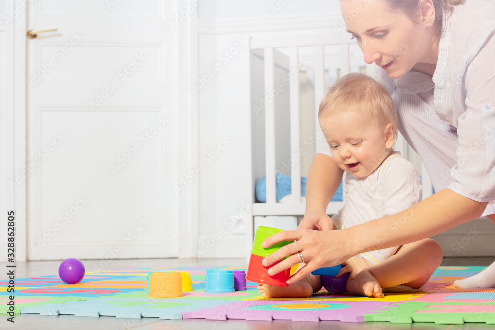 Mom play with baby toddler boy building pyramids on the carpet in nursery by the child crib Mom play with baby toddler boy building pyramids on the carpet in nursery by the child crib
