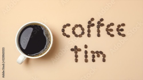 Top view of stop motion roasted coffee beans arranged in letters and hot coffee in white coffee cup on light brown background for coffee menus or coffee shop signs. 4K resolution ultra HD.