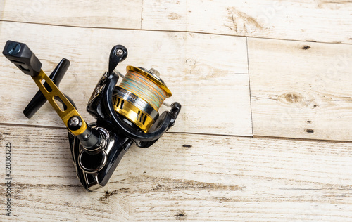 Golden fishing reel on wooden floor, equipment with pe line, rust-proof technology, ball bearing system photo