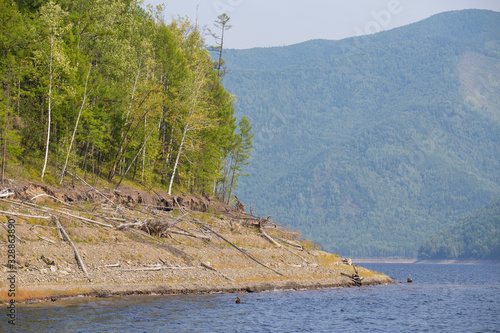 Beautiful landscape. Zeya reservoir, Amur region. A beautiful rocky shore with tall green trees goes into the calm blue waters of the reservoir. photo