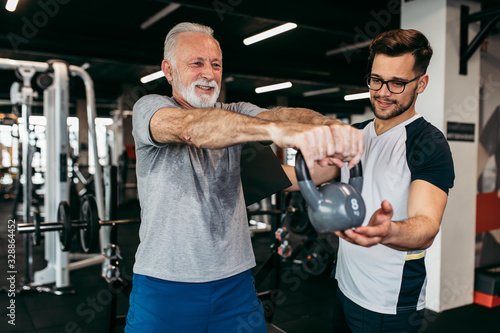 Fototapeta Senior man exercising in gym with his personal trainer.
