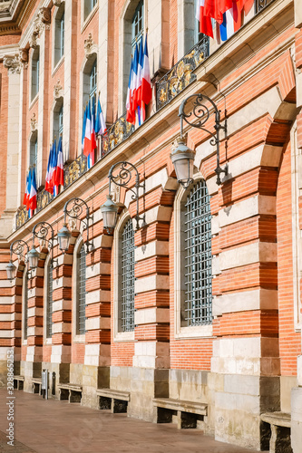 The Capitole. City hall of Toulouse with its monumental brick classic facade, richly adorned with French flags