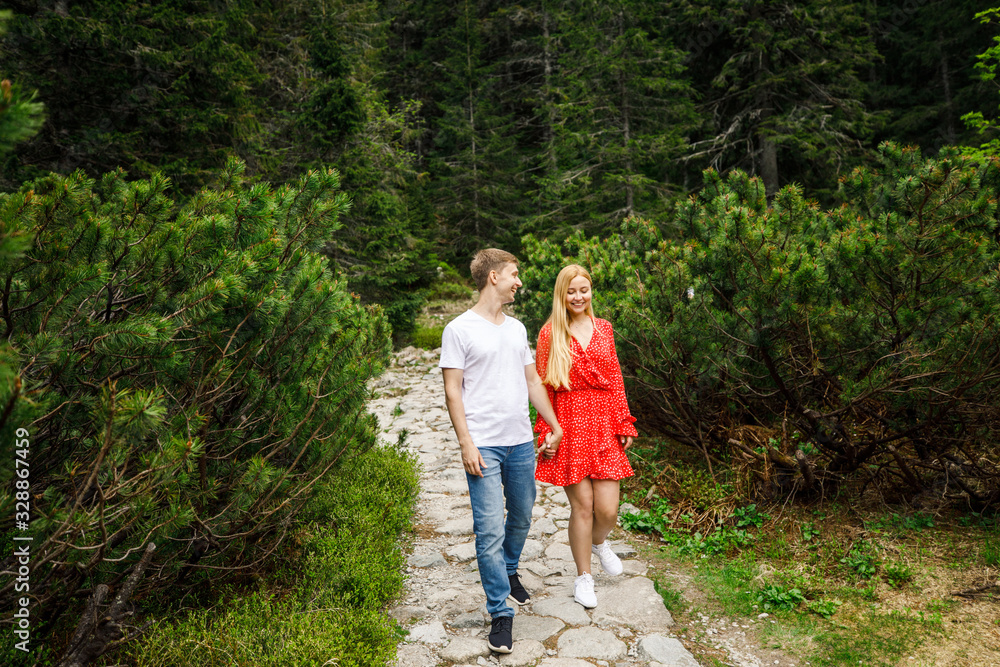 a young couple, a girl in a red dress, and a man in a white T-shirt and blue pants, are walking in the Tatra National Park in Poland