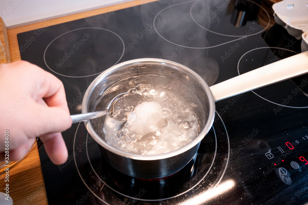 Ein hühner ei wird mit einem löffel in einen topf mit kochendem wasser gelegt Ein hühner ei wird mit einem löffel in einen topf mit kochendem wasser gelegt