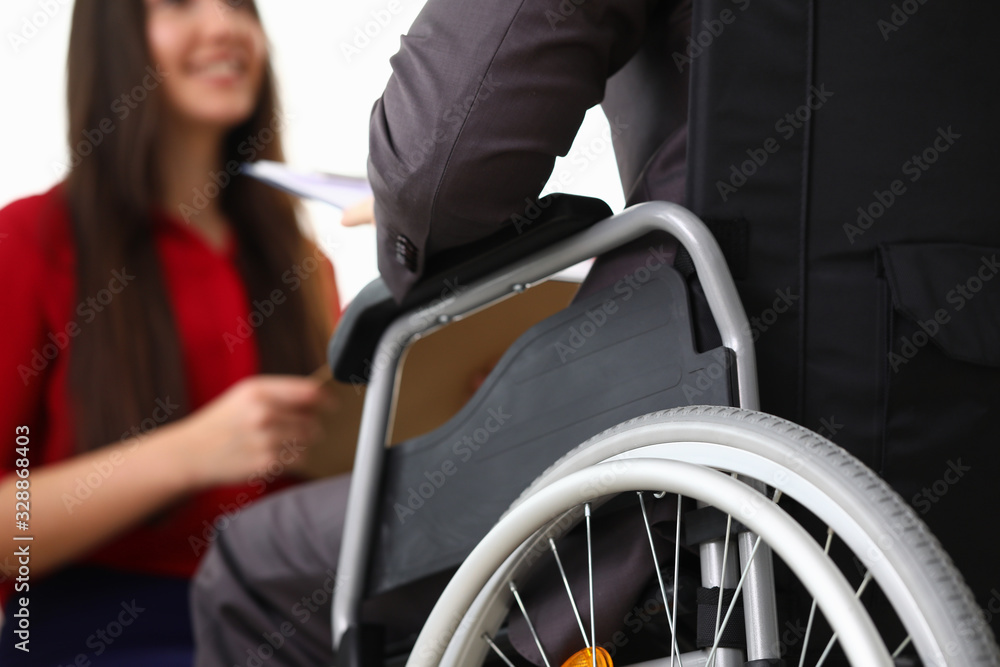 Obraz premium Close-up view of smiling businesswoman interviewing disabled candidate in office. Male in disabled carriage. Adaptation of people with disabilities in society concept