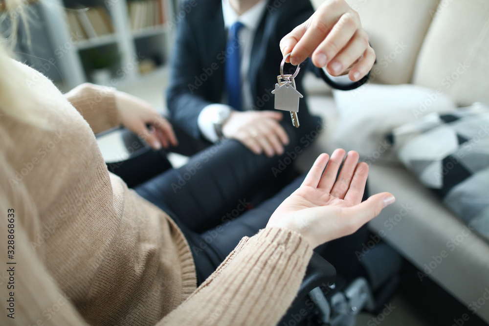 Close-up of client and realtor. Agent giving keys of apartment to new owner in disabled carriage after signed lease agreement. Real estate concept. Adaptation of people with disabilities in society