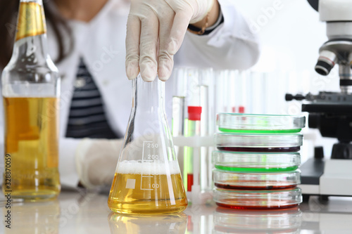 Close-up of assistant hands pouring yellow liquid into flask. Professional scientist making mixture of fluid for experiment. Chemical researching and quality test concept