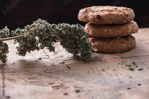 three cookies with marijuana lie on top of each other on a wooden board. Near big bud cannabis. Horizontal photo