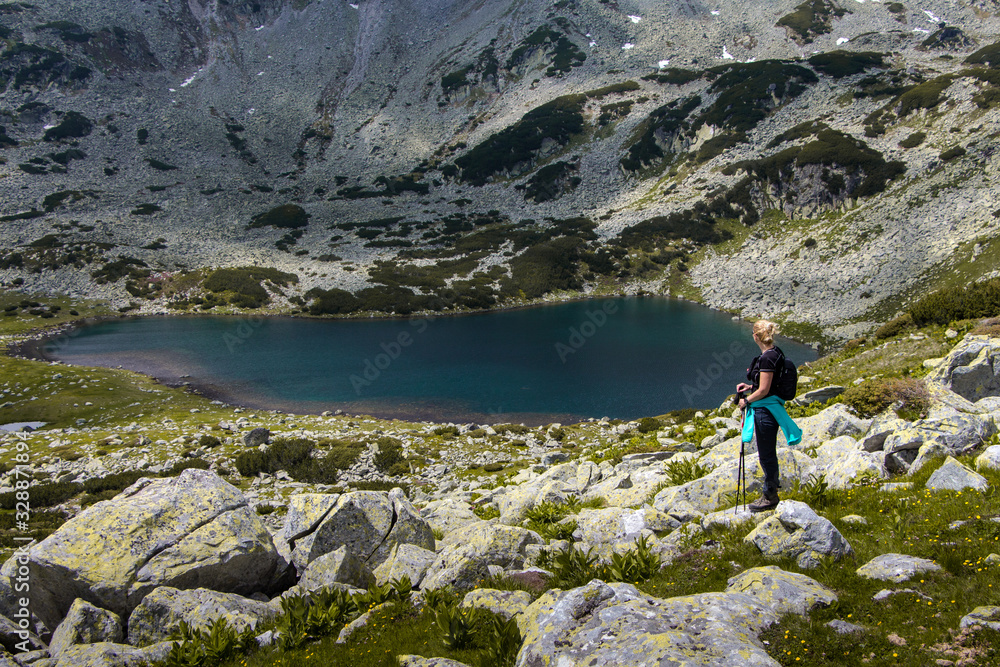 Naklejka premium Young hiker woman standing on the lakeside, Retezat mountain range, Romania. Freedom and beauty in nature
