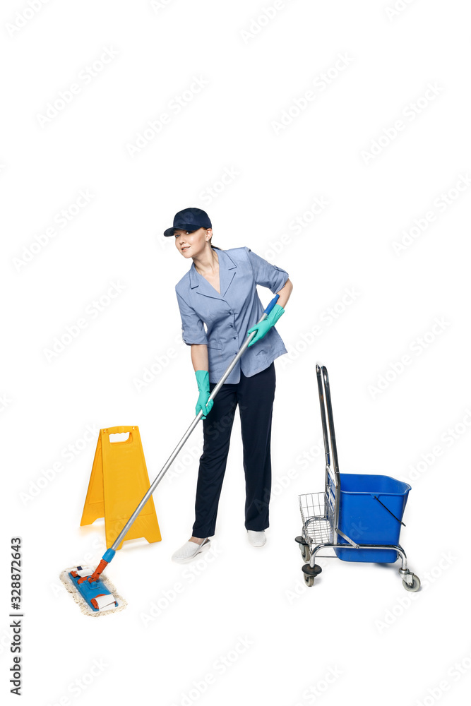 Girl in a cleaning uniform with a mop and a bucket on wheels, isolated on white background and a wet floor sign Girl in a cleaning uniform with a mop and a bucket on wheels, isolated on white background and a wet floor sign