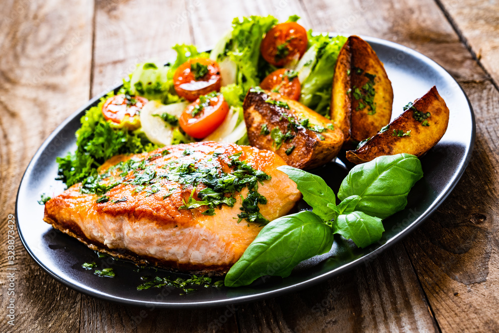 Fried salmon steak with potatoes and vegetables on wooden table Fried salmon steak with potatoes and vegetables on wooden table