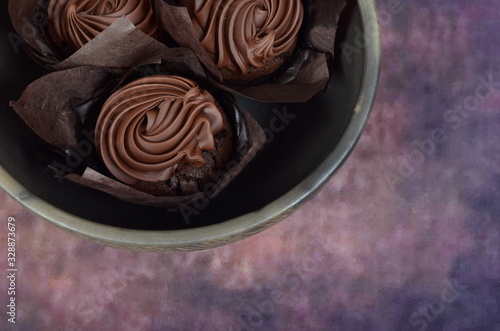 Three chocolate muffins in a clay bowl on a colored background