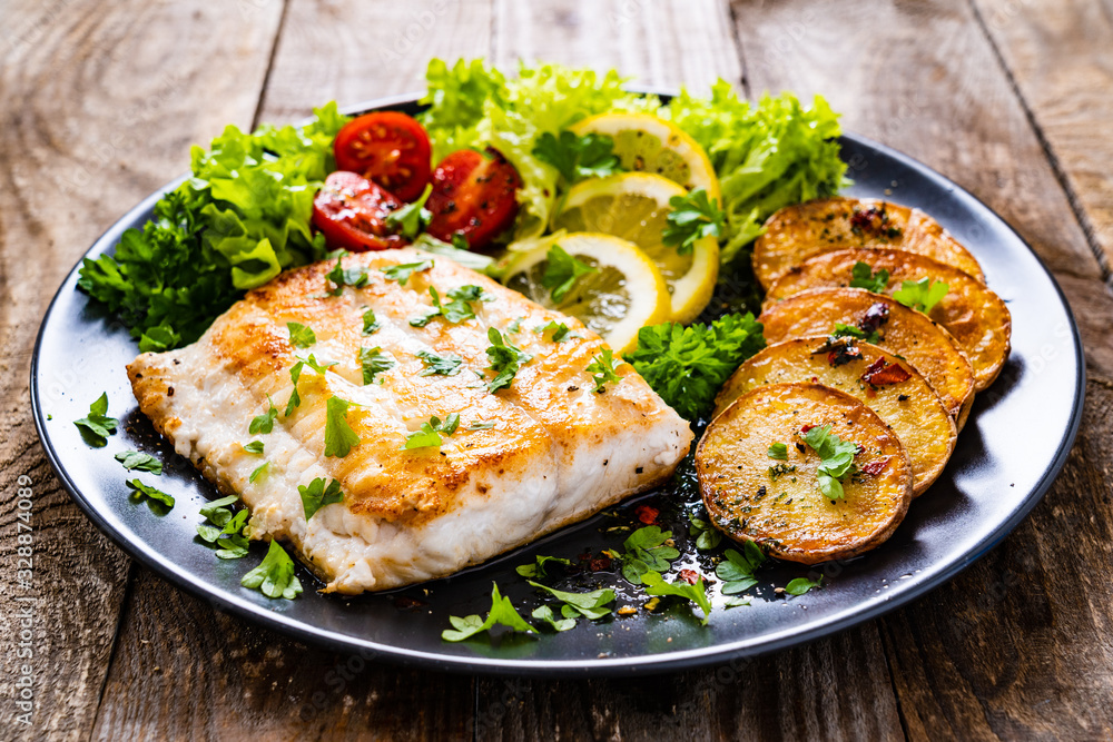 Fish dish - fried cod fillet with potatoes and vegetables on wooden table Fish dish - fried cod fillet with potatoes and vegetables on wooden table