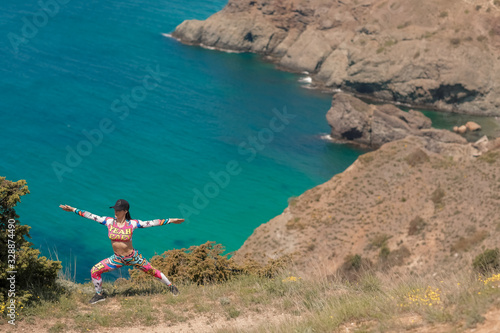 Sportswoman near the sea coast on the mountain trains and warms up in sportswear