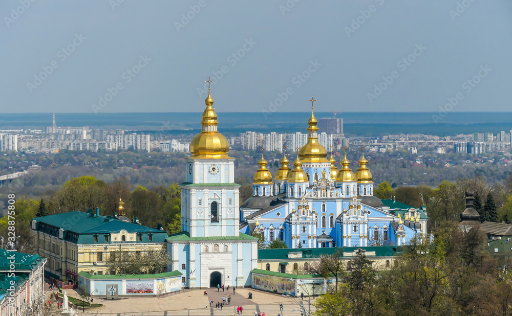 Distanced view on St Michael's Golden-Domed Cathedral in Kiev, Ukraine. The walls of the cathedral are painted blue and nicely decorated on each facade. Golden domes are reflecting the strong sun.