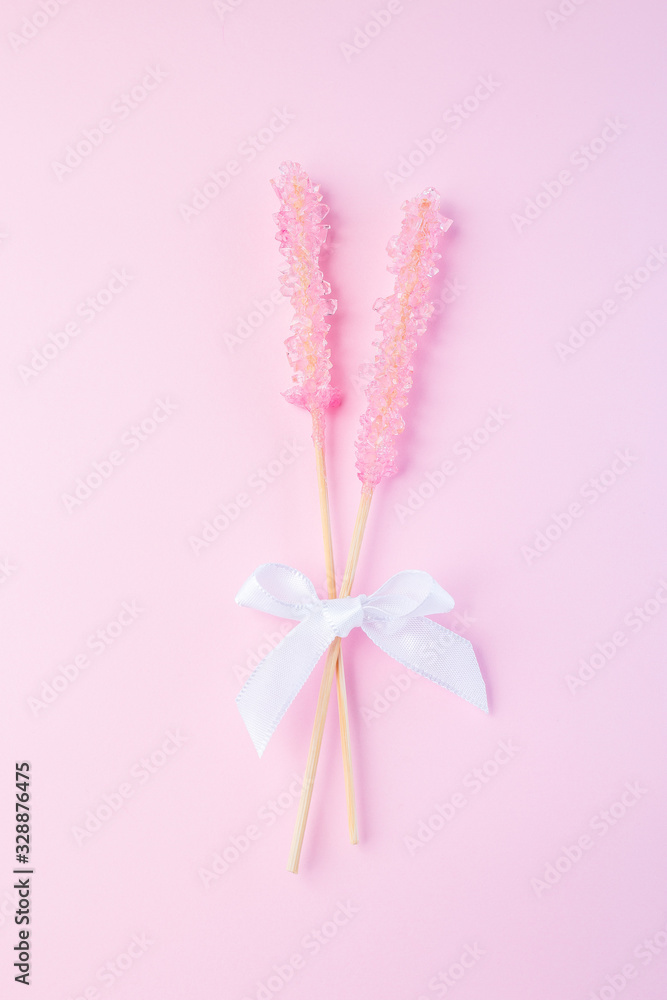 Two pink rock candy on pink paper background decorated with a white bow, vertical, top view Two pink rock candy on pink paper background decorated with a white bow, vertical, top view