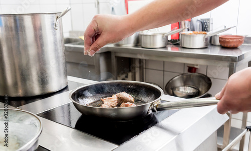 Chef cooks fried potatoes with pieces of meat in a restaurant kitchen