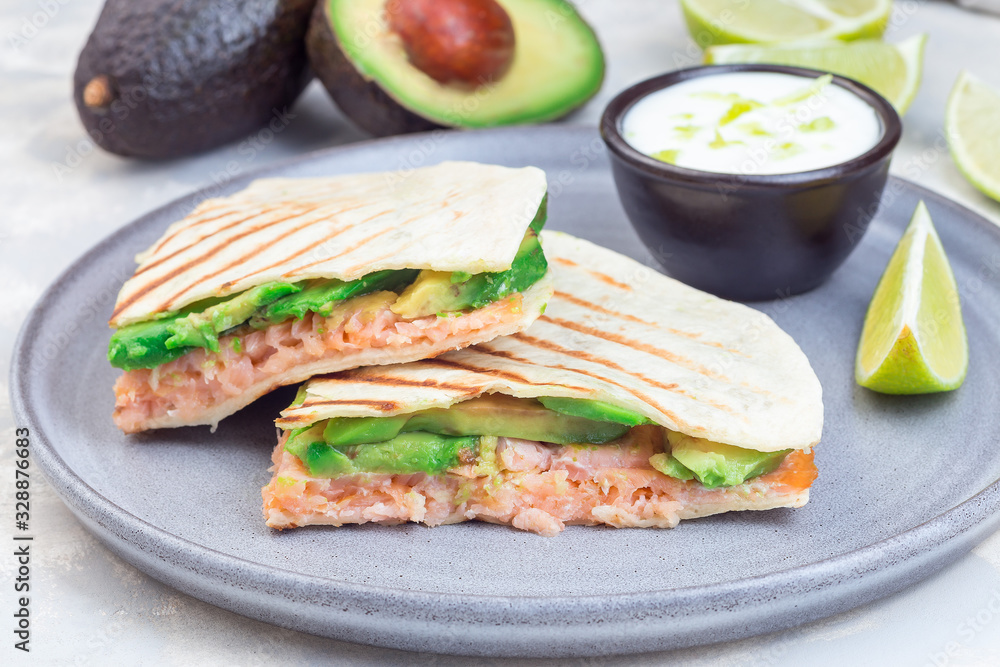Grilled quesadilla with smoked salmon and avocado served with yogurt and lime dip, on gray plate, horizontal