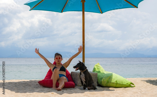 outdoors portrait of young happy and attractive Asian Korean woman in bikini at beautiful beach relaxed and cheerful together with her dog enjoying summer holidays