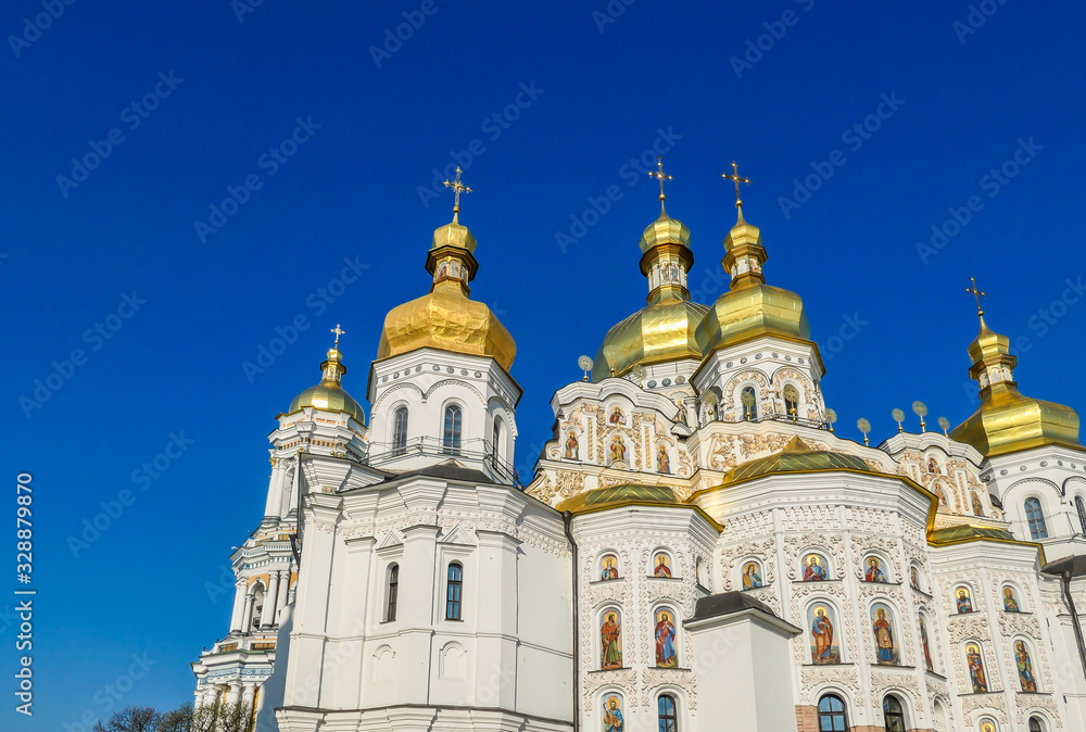 A close-up view on Pechersk Lavra in Kiev, Ukraine, known as the Kiev Monastery of the Caves. It is a historic Orthodox Christian monastery. Green rooftops with golden domes. Walls are painted white.