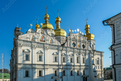 A close-up view on Pechersk Lavra in Kiev, Ukraine, known as the Kiev Monastery of the Caves. It is a historic Orthodox Christian monastery. Green rooftops with golden domes. Walls are painted white. © Chris