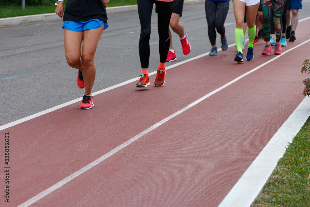 A group of athletes running on a track in a park. Only legs are visible.