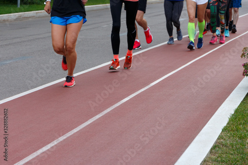 A group of athletes running on a track in a park. Only legs are visible.