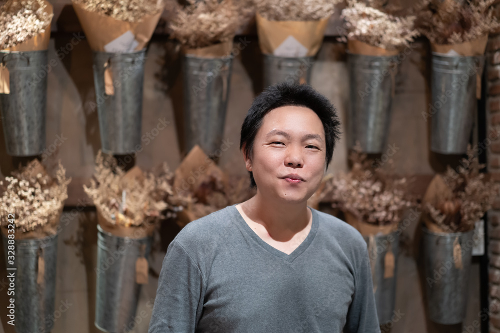 Happy Asian Adult man smiles to the camera in front of vertical dried flower in aluminum pot on the wall.