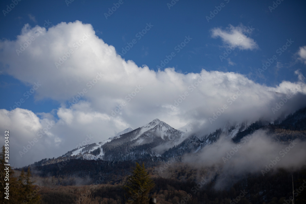 Mountain landscape in early spring. The fog slides from the mountains. Snow peaks. Ski resort. Beautiful highland background. Wide view of the mountain range. The calm of northern nature.