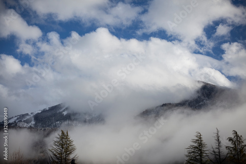 Fototapeta Naklejka Na Ścianę i Meble -  Mountain landscape in early spring. The fog slides from the mountains. Snow peaks. Ski resort. Beautiful highland background. Wide view of the mountain range. The calm of northern nature.