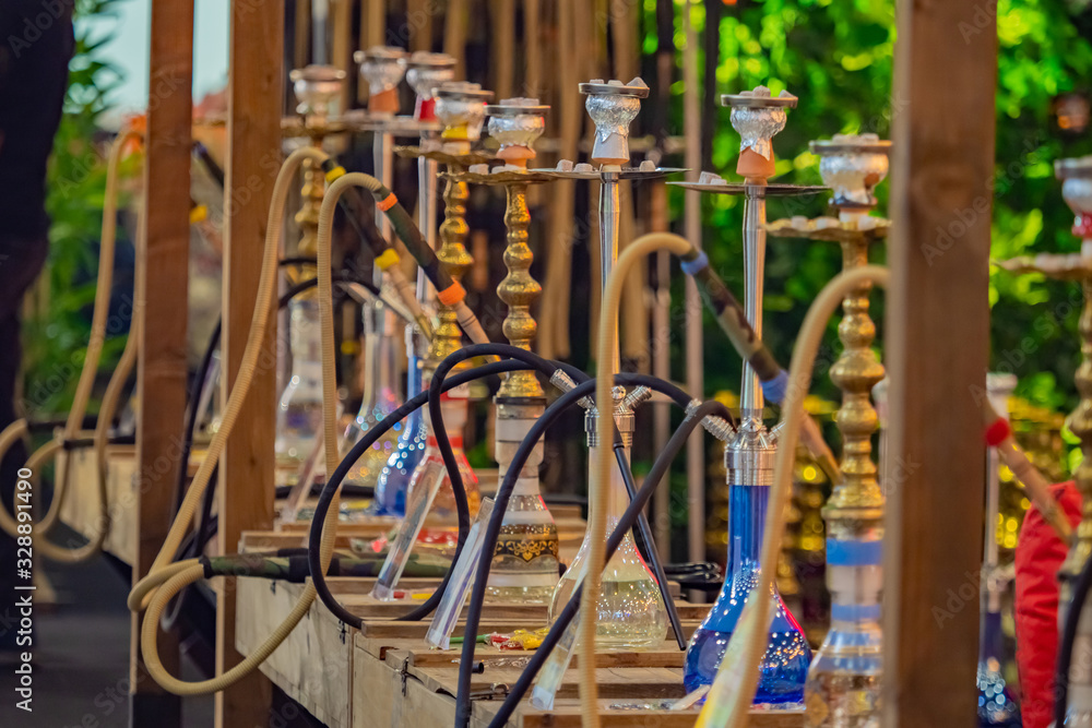 Several hookahs are standing on the street. Multi-colored hookahs on a wooden rack. Concept - hookah shop. Hookah party takes place on the street. Hookah of different types exhibited on the street Several hookahs are standing on the street. Multi-colored hookahs on a wooden rack. Concept - hookah shop. Hookah party takes place on the street. Hookah of different types exhibited on the street