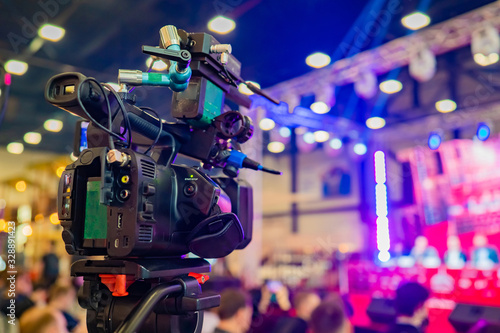 The professional camera is aimed at the scene. Professional camera on a tripod. Camera for video shooting near the audience. Concept - organization of video filming. Professional video shooting