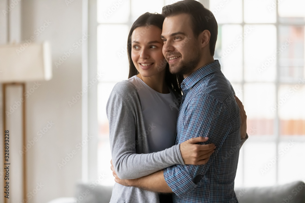 Head shot loving married couple cuddling, looking away. Affectionate caring young spouses homeowners embracing, enjoying sweet tender moment together, planning visualizing future at new home. Head shot loving married couple cuddling, looking away. Affectionate caring young spouses homeowners embracing, enjoying sweet tender moment together, planning visualizing future at new home.