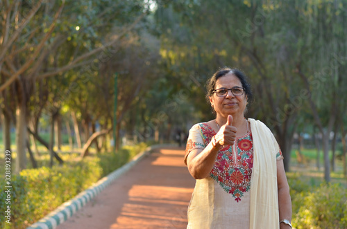 Wallpaper Mural Portrait shot of a happy looking senior north Indian woman wearing traditional chikan kari Indian salwar kameez showing a thumbs up in a garden against a bokeh of canopy of trees. Torontodigital.ca