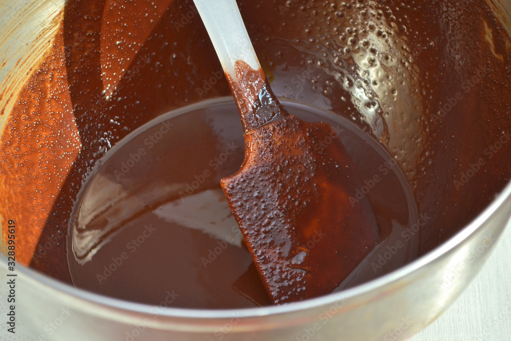 Melted delicious brown chocolate in a metal bowl for future handmade sweets, with a mixing spatula Melted delicious brown chocolate in a metal bowl for future handmade sweets, with a mixing spatula