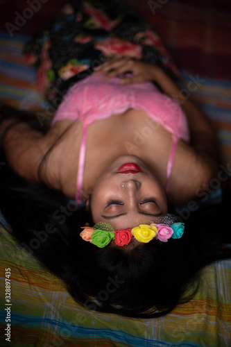 Top view of an Asian/Japanese/Korean brunette young girl in pink inner wear and floral headband lying on bed inside of a room. Fashion and boudoir photography.
