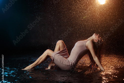 Beautiful sexy girl with drops of water on her face in splashes illuminated by an orange light against a dark background in the studio.