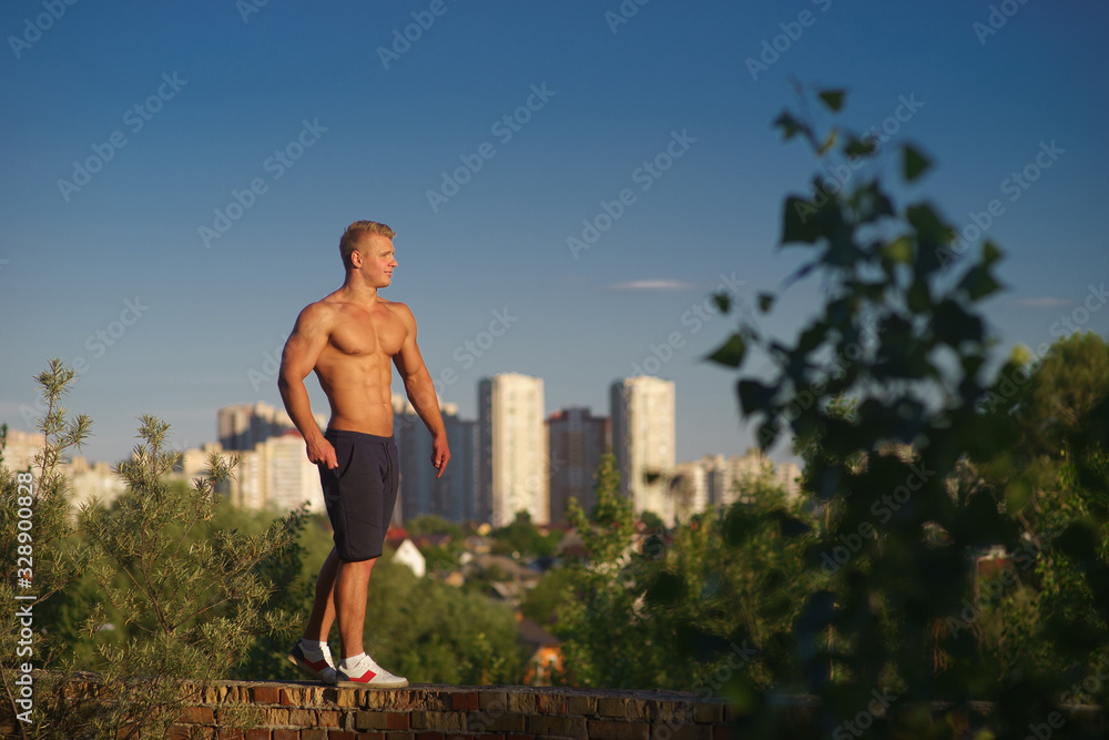 Muscular young man standing on top of the roof and looking at during sunset. Concept of healthy lifestyle and confident 