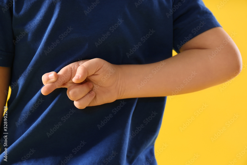 Little boy with crossed fingers on yellow background, closeup. April fool's day
