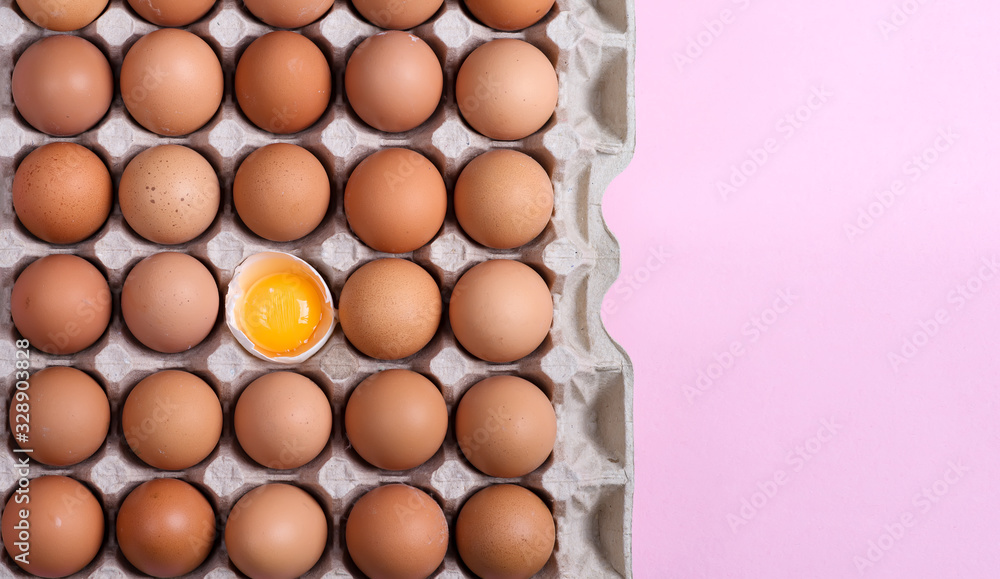 Papercraft eco box with fresh natural chicken eggs and one yolk in a shell on a light pink background. Papercraft eco box with fresh natural chicken eggs and one yolk in a shell on a light pink background.