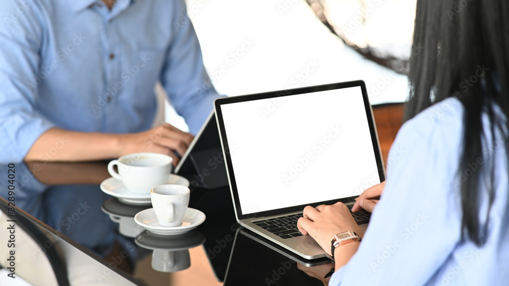 Cropped image of business development team working/using a computer tablet and laptop with white blank screen while sitting together at the modern working table with orderly workplace as background. Cropped image of business development team working/using a computer tablet and laptop with white blank screen while sitting together at the modern working table with orderly workplace as background.