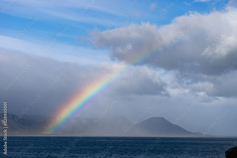 Beautiful summer landscape with sea, small village on the hill, bright colorful rainbow on blue sky, clouds and mountains on the horizon. Iceland, Peninsula Beautiful summer landscape with sea, small village on the hill, bright colorful rainbow on blue sky, clouds and mountains on the horizon. Iceland, Peninsula