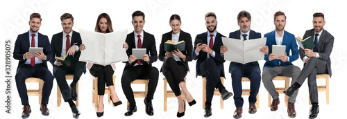 Team of 9 businessmen reading from books, newspaper, tablets and phones