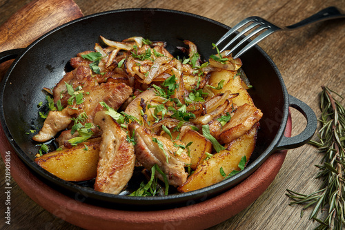 Fried potatoes with bacon, onions and herbs in a decorative pan on a wooden background. Close up, selective focus.