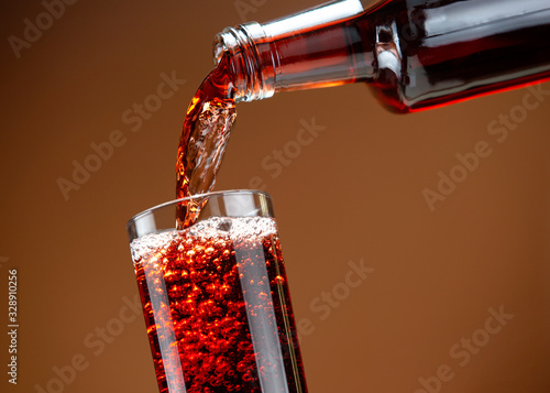 Carbonated cherry drink pouring from a bottle into a glass