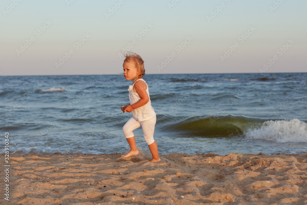 Little beautiful girl frolic on the sandy seashore.