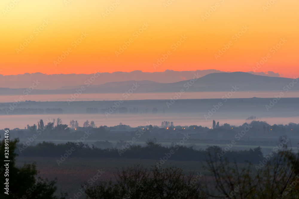 layered rural landscape with sunset colours and mist, giving a feeling of heat and the peak of summer.
