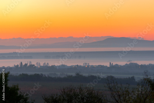 layered rural landscape with sunset colours and mist, giving a feeling of heat and the peak of summer. © Kostas